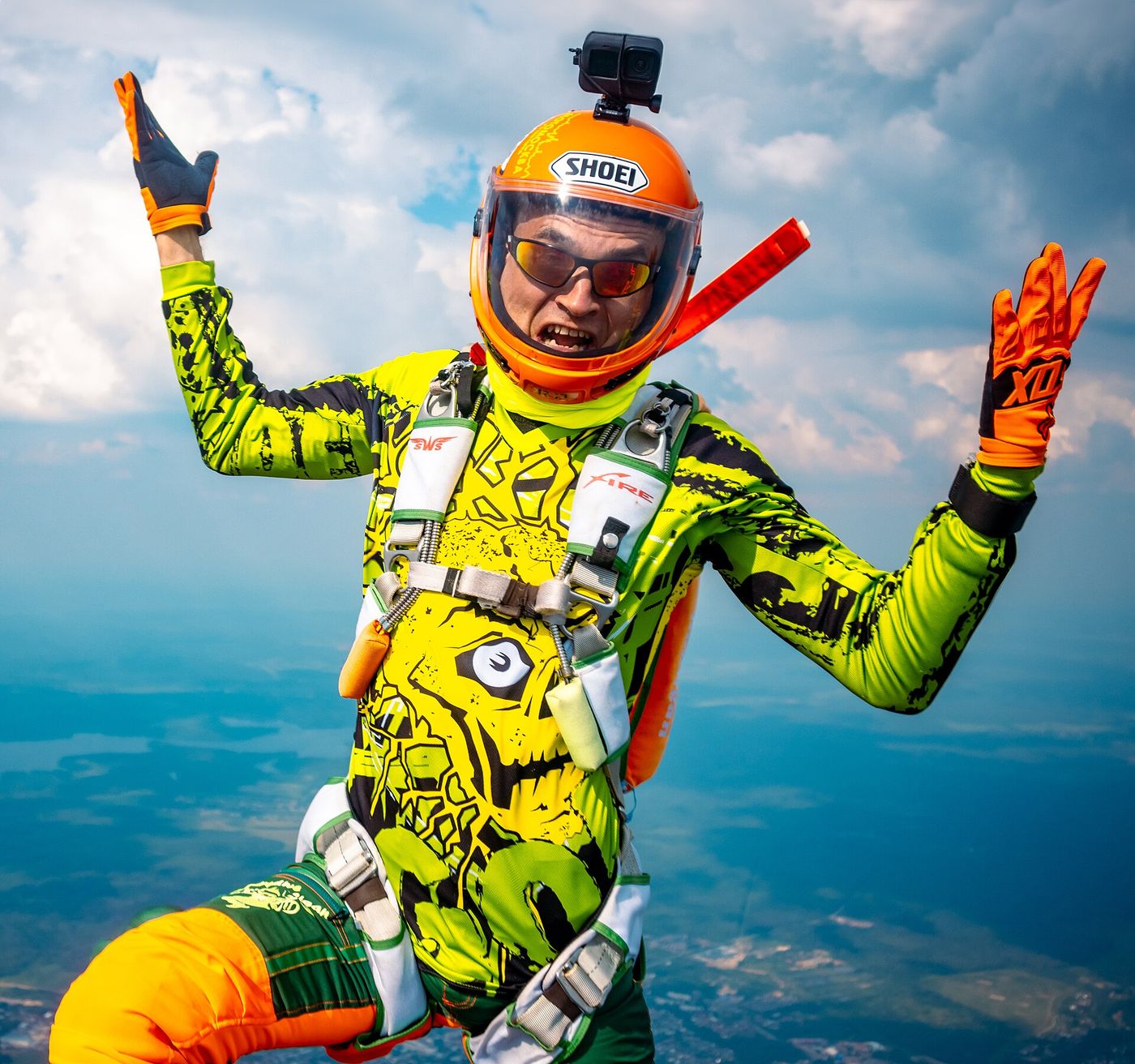 Skydiver in a bright green custom suit and orange helmet grinning at the camera in freefall