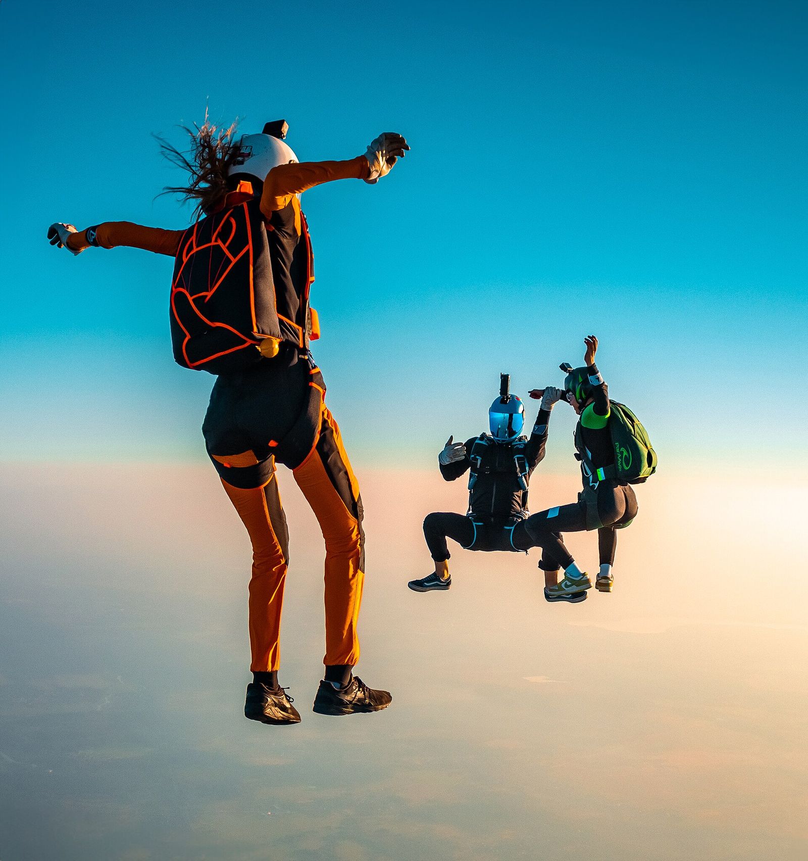 Three skydivers in freefall formation at sunset