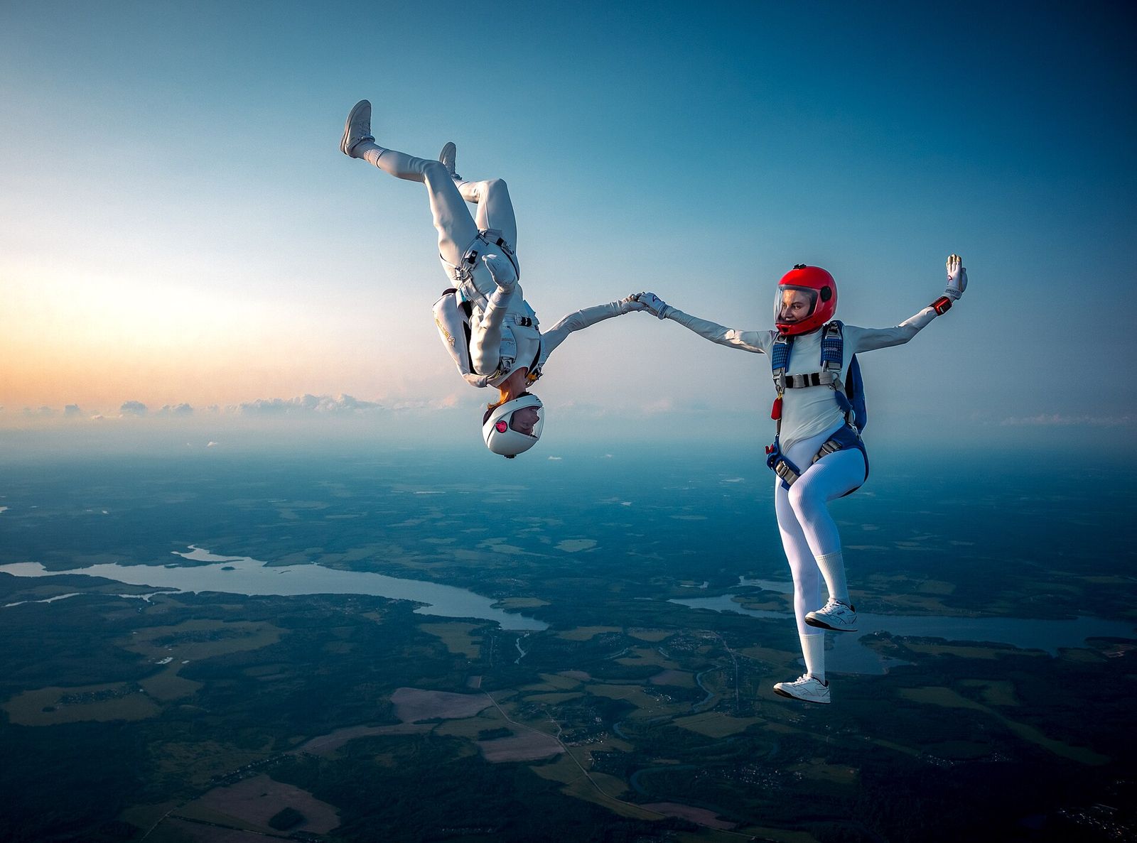 Two skydivers in white suits linked in freefall above a river valley